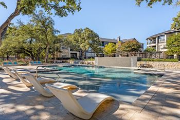A pool surrounded by lounge chairs and trees. at Preserve at Rolling Oaks, Austin